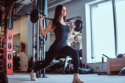 beautiful-brunette-female-sportswear-doing-lunge-with-barbell-fitness-club-gym